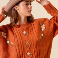 Brick cable-knit sweater detail with embroidered daisy flowers and diamond motifs