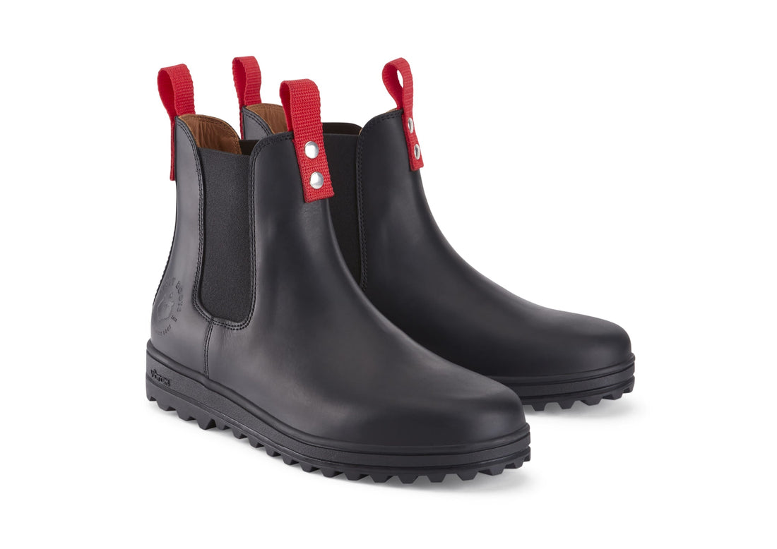 Pair of black leather Chelsea boots with red pull tabs and thick lug soles.