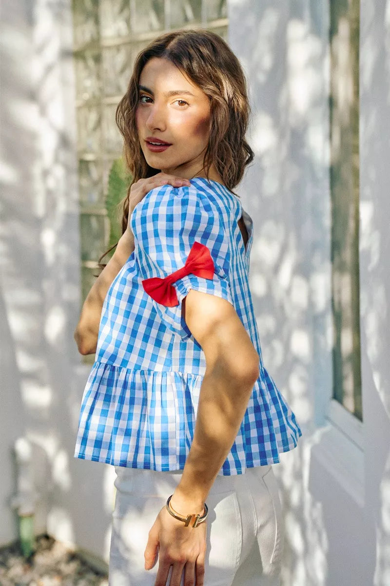 Blue gingham short-sleeve blouse with red ribbon bow detail at the shoulder and waist peplum