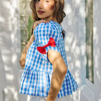 Blue gingham short-sleeve blouse with red ribbon bow detail at the shoulder and waist peplum