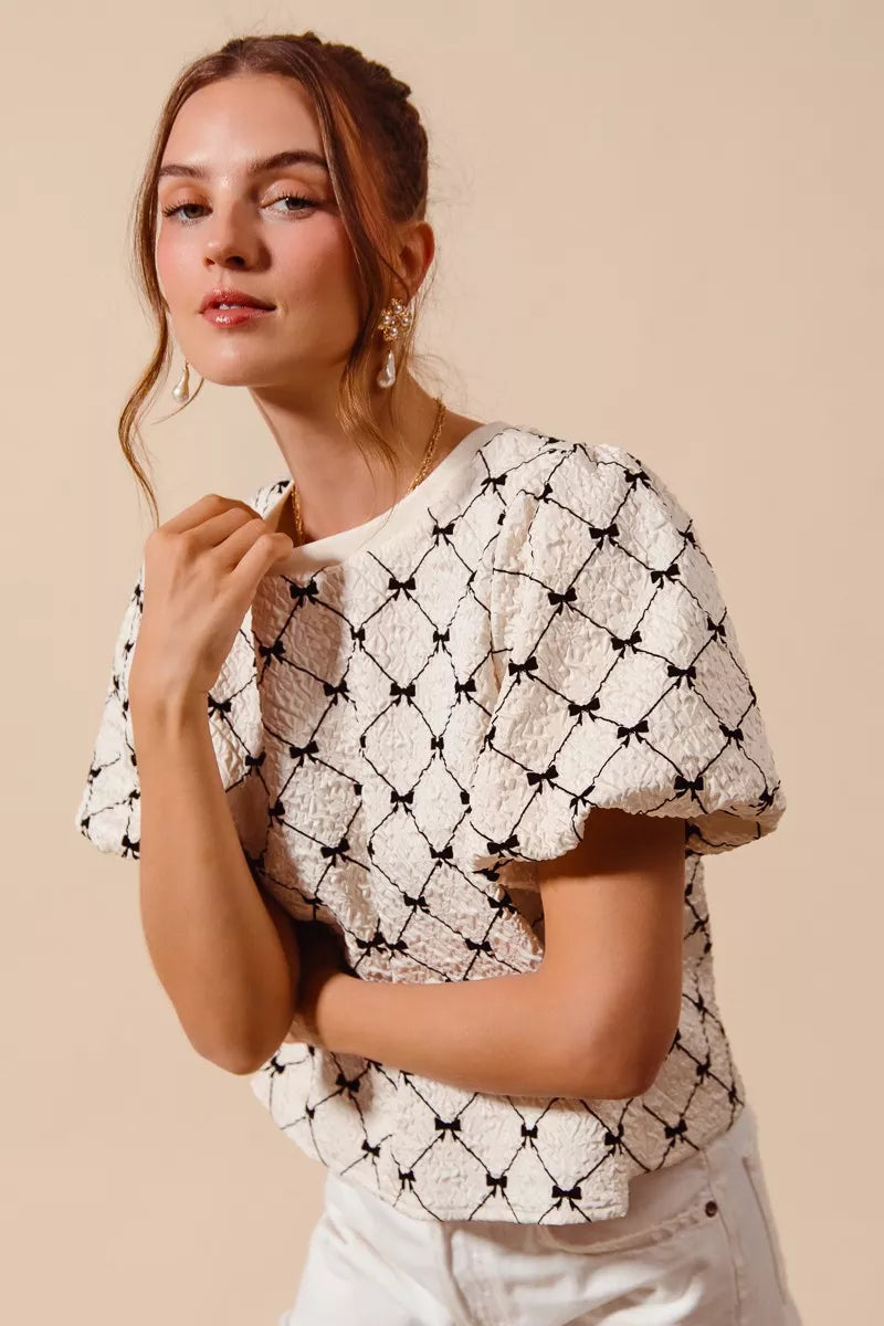 Ivory woven bubble sleeve top with black bow texture pattern, close side profile