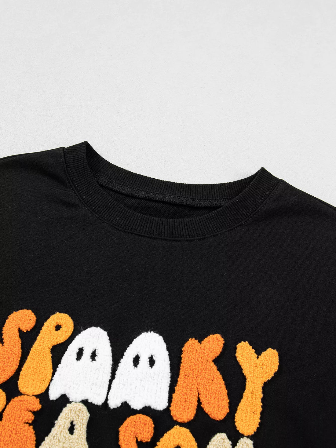 Close-up of black crewneck sweatshirt neckline with partial embroidered graphic