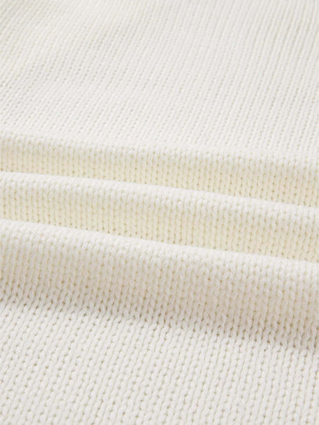 Close-up of off-white knit cardigan hem ribbing and textured sweater knit.