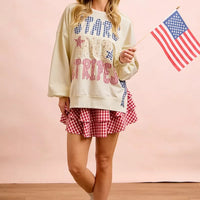 Cream sweatshirt with star-and-stripe patch graphic and blue bow detail near lower hem.