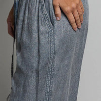 Charcoal wide-leg woven pants close-up: embroidered panels and tassel drawstring