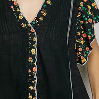 Close-up of black V-neck blouse with floral trim and pintuck front seam