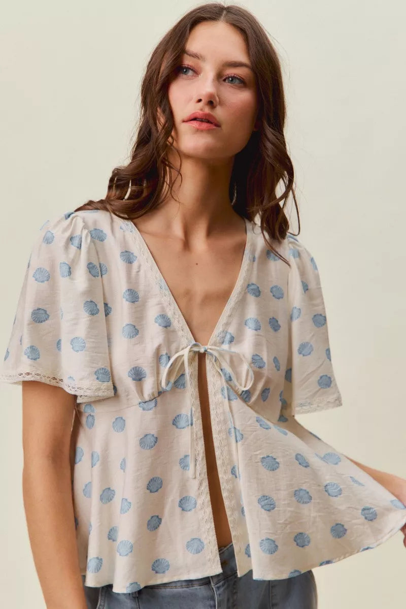 Ivory dot-print blouse with tie-front V-neck and flowing flutter sleeves.