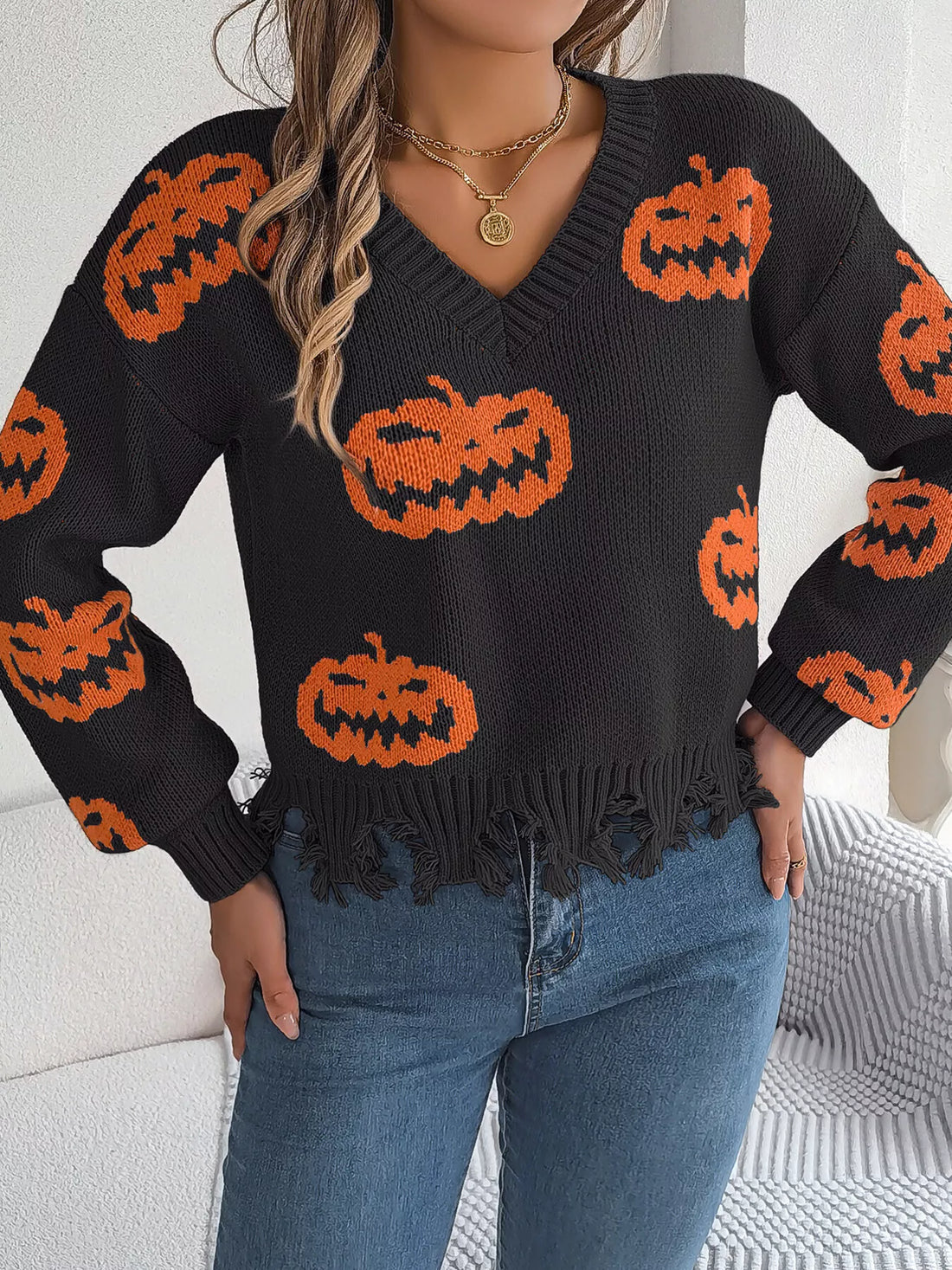Black knit pumpkin sweater with orange jack-o’-lanterns, V-neck, and distressed hem fringe