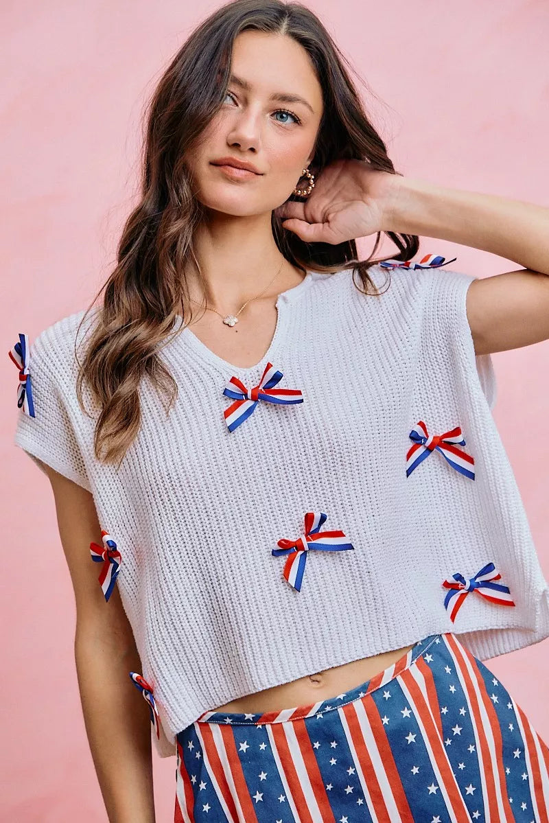 Off-white dolman sweater top with red, white, and blue bow appliques across the chest