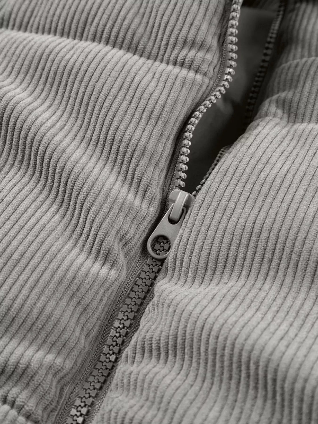 Gray corduroy puffer vest zipper close-up with visible zipper pull and stitched placket.