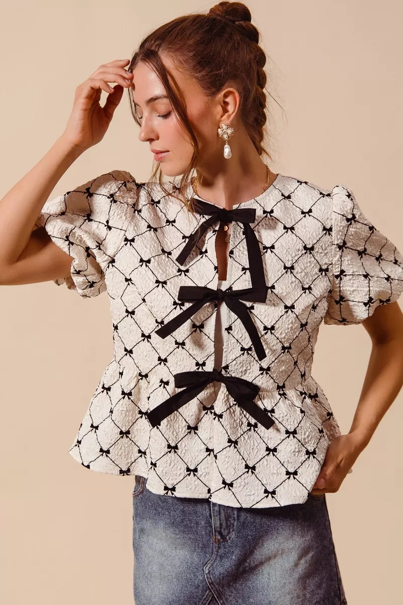 Ivory woven peplum top with black bow tie at neckline and puff sleeves, side view.