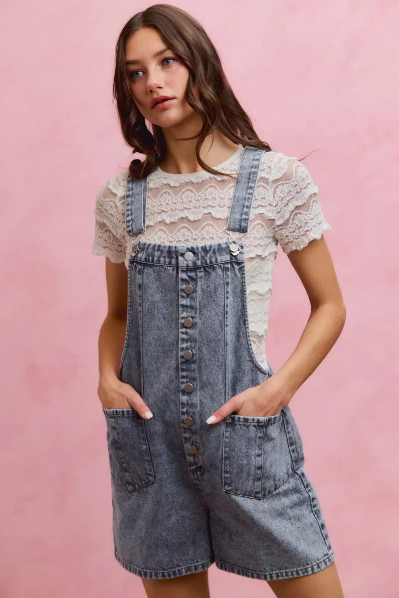 Light wash denim overall romper with adjustable straps, front buttons, and large front pocket
