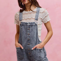 Light wash denim overall romper with adjustable straps, front buttons, and large front pocket