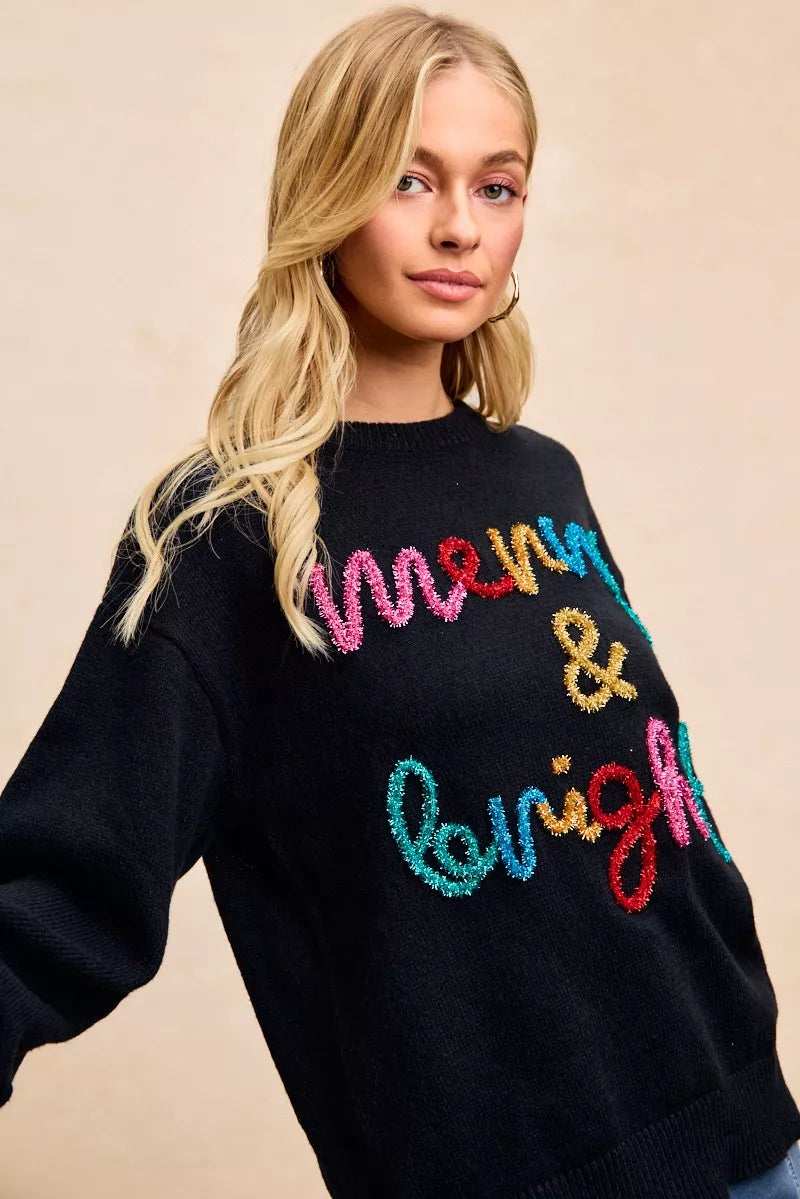 Black sweater with multicolor tinsel "Merry & bright" lettering across the chest.