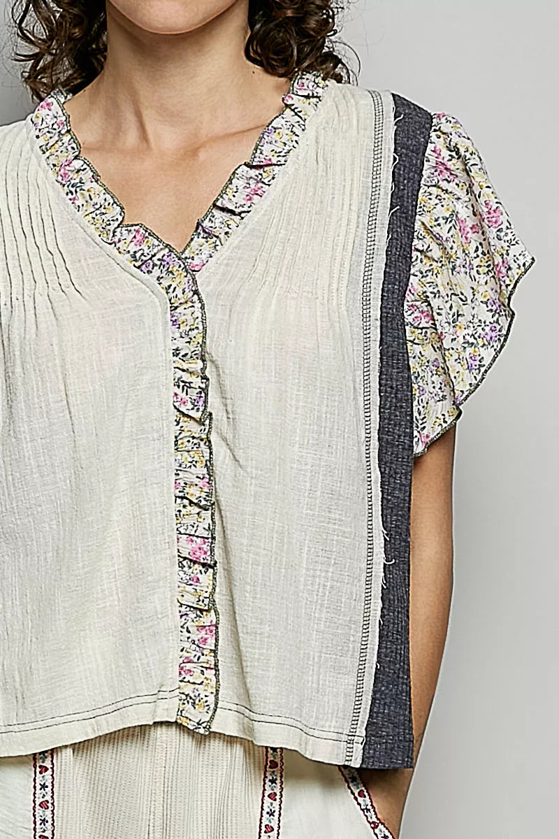 Cream V-neck blouse close-up with floral ruffle trim and textured placket