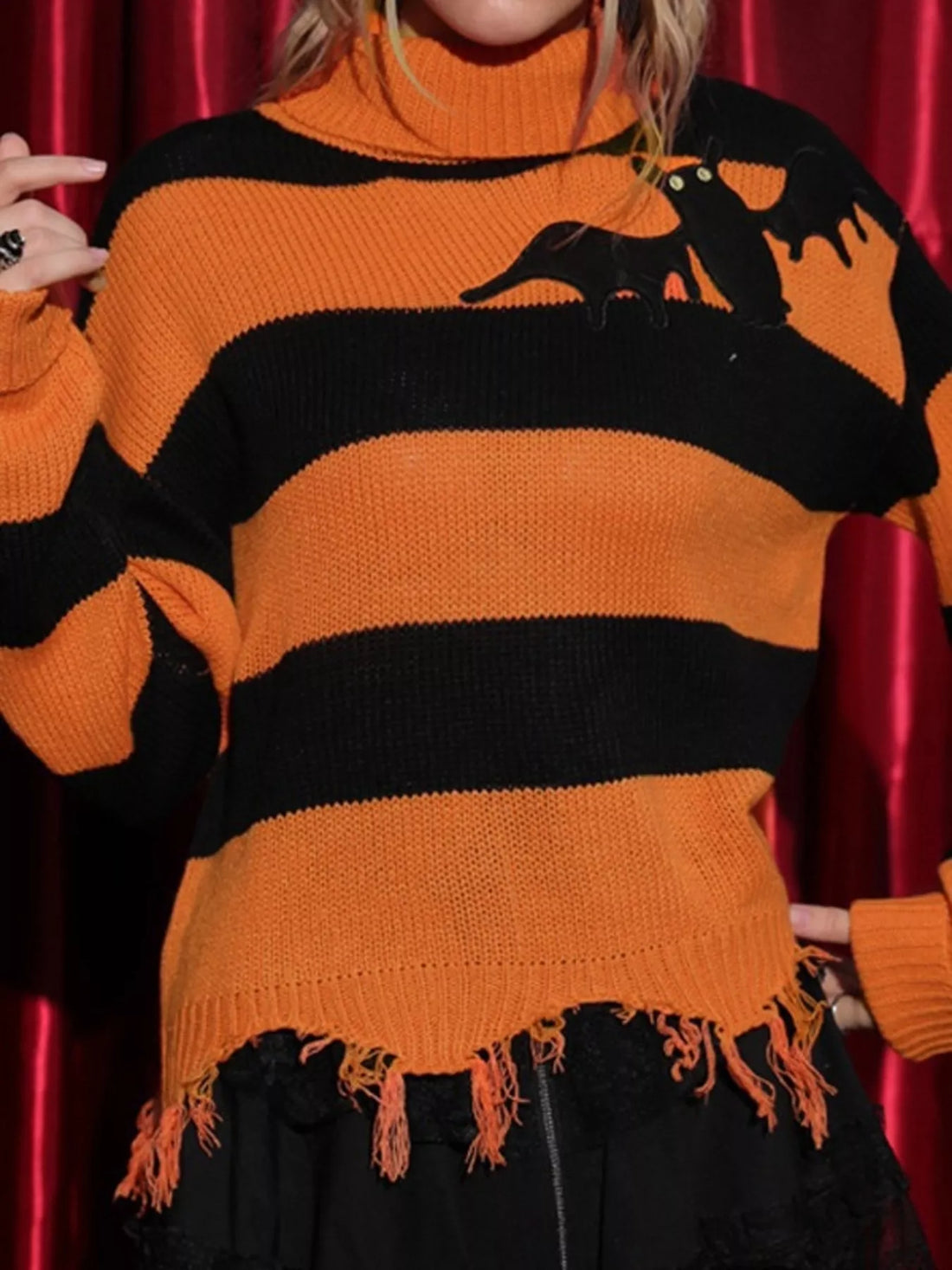 Orange and black striped turtleneck sweater with bat graphic, ribbed cuffs, fringe hem