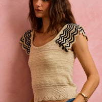 Oatmeal knit top with wavy texture, flutter sleeves, and black zigzag trim