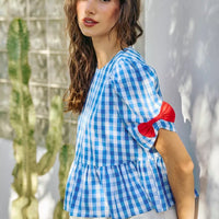 Blue gingham peplum blouse with short puff sleeves and red bows on the upper sleeves