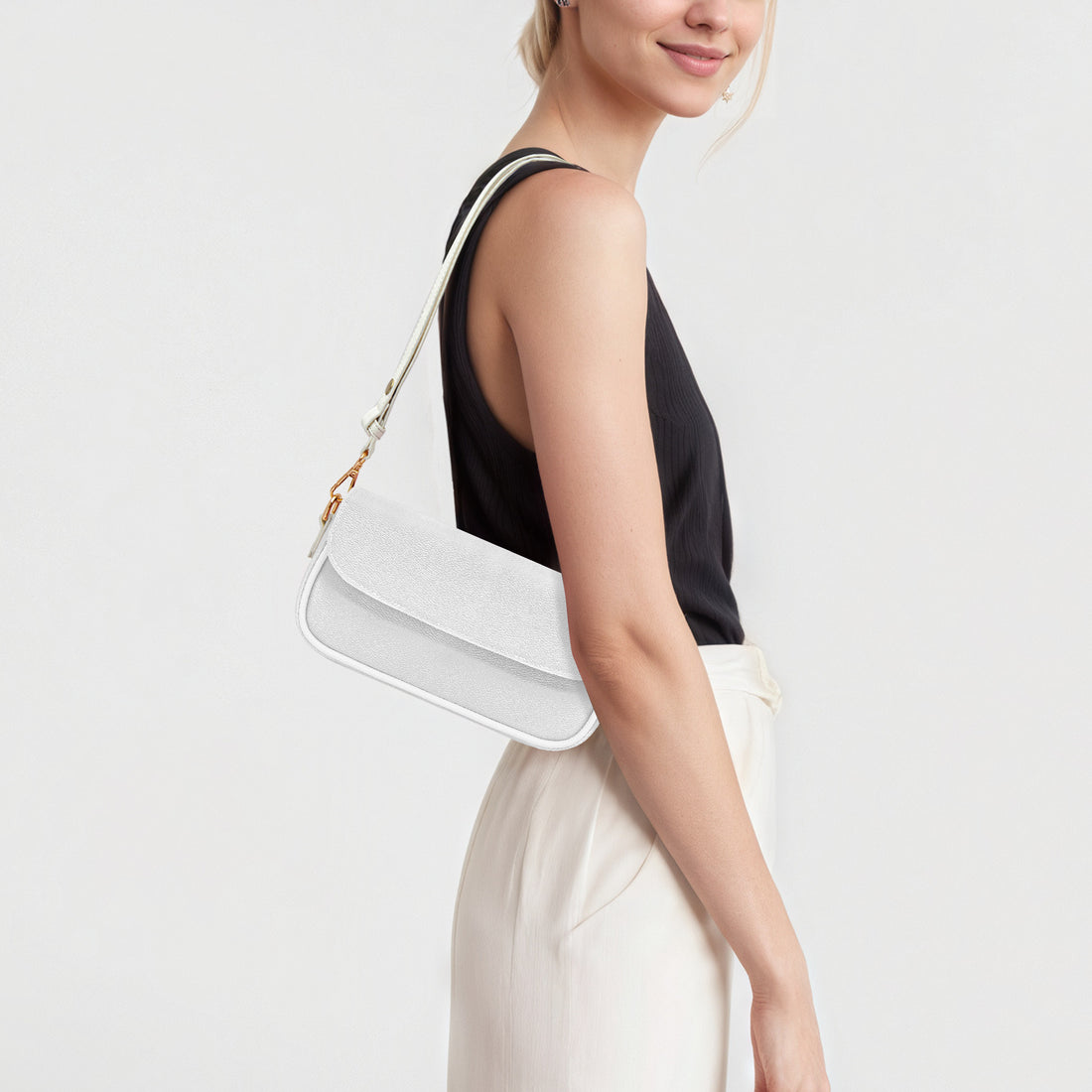 White mini shoulder bag worn at shoulder with gold chain strap and flap.
