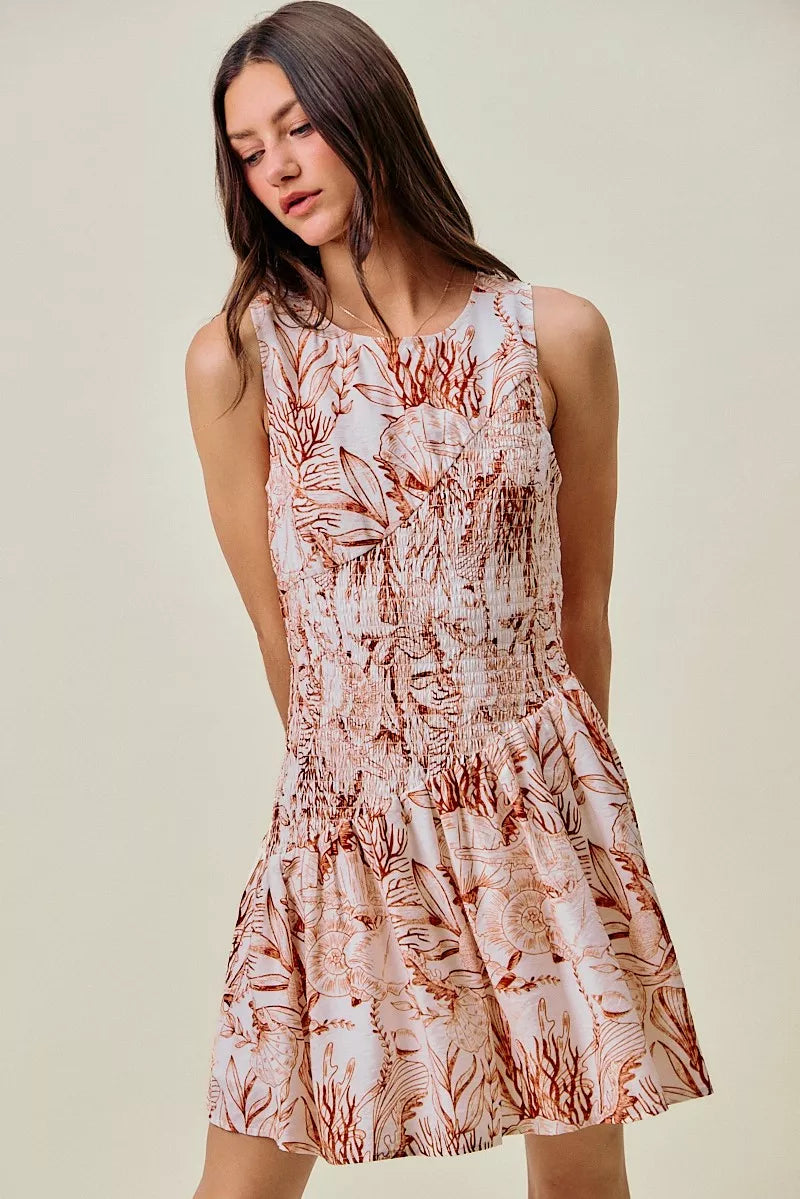 Lined sleeveless mini dress with smocked bodice and coral-brown shell print, tiered skirt