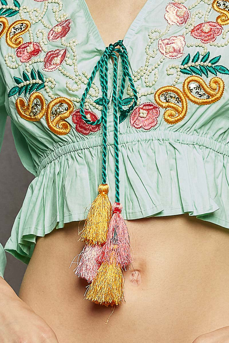 Detail of mint floral embroidered blouse bodice with tassel drawstring tie
