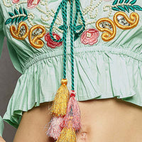 Detail of mint floral embroidered blouse bodice with tassel drawstring tie