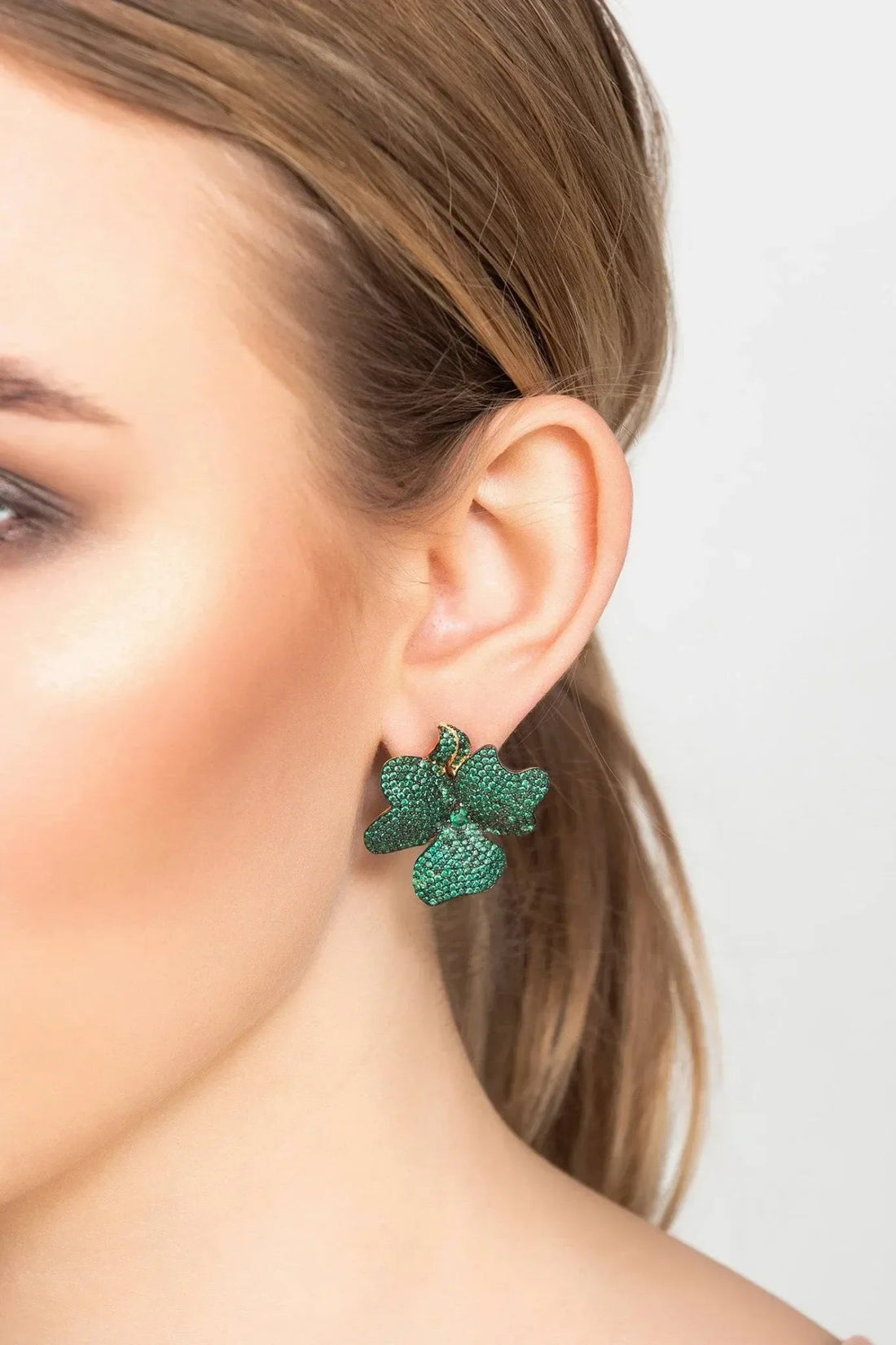 Flower stud earrings with emerald green stones and gold-toned posts worn on ear