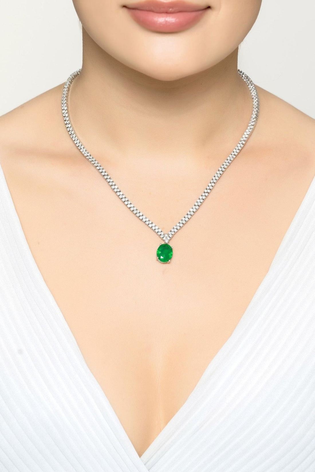 Silver tennis necklace with oval emerald pendant worn on a model