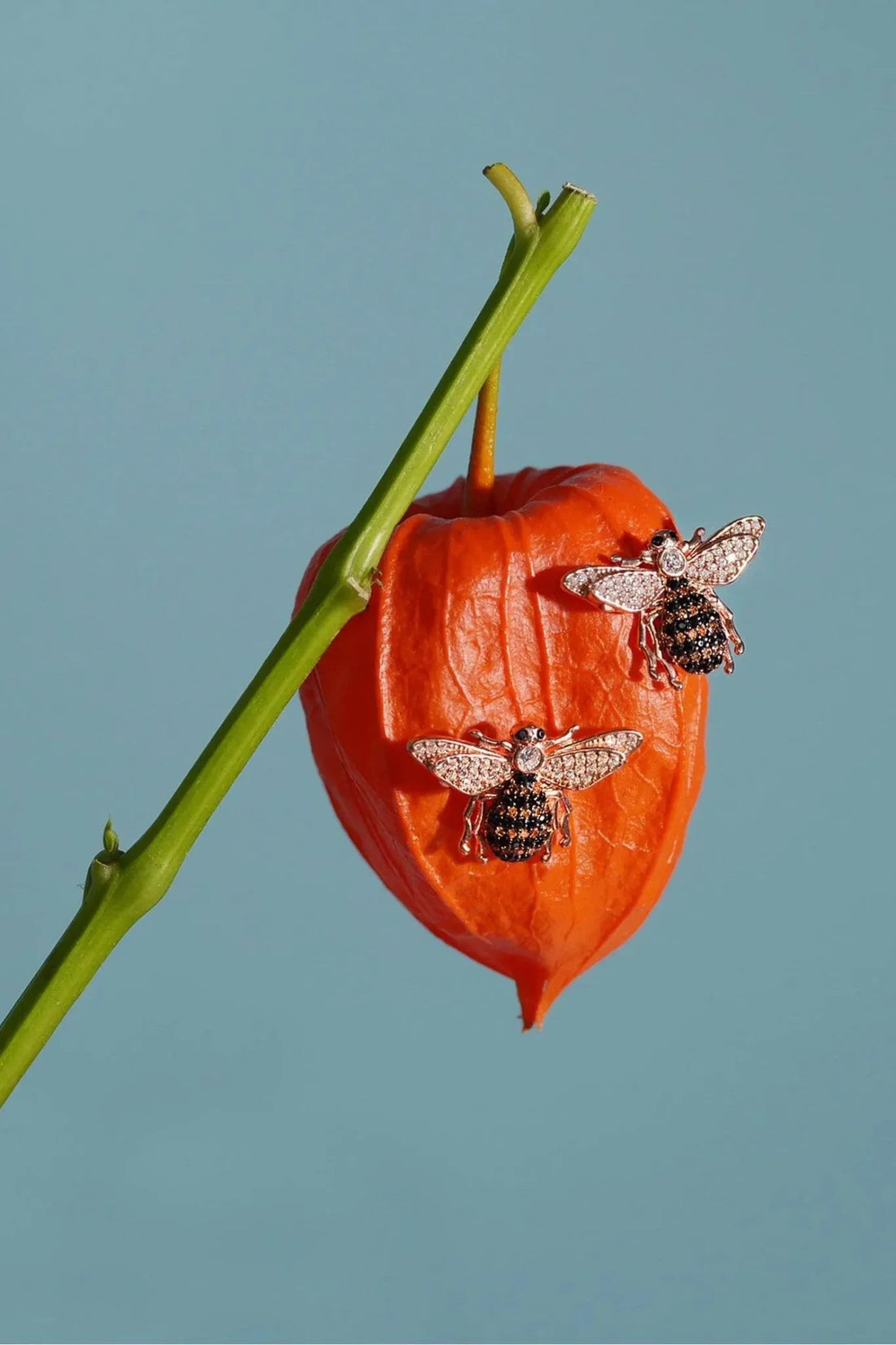 Silver honey bee stud earring resting on red chili pepper, crystal wing details