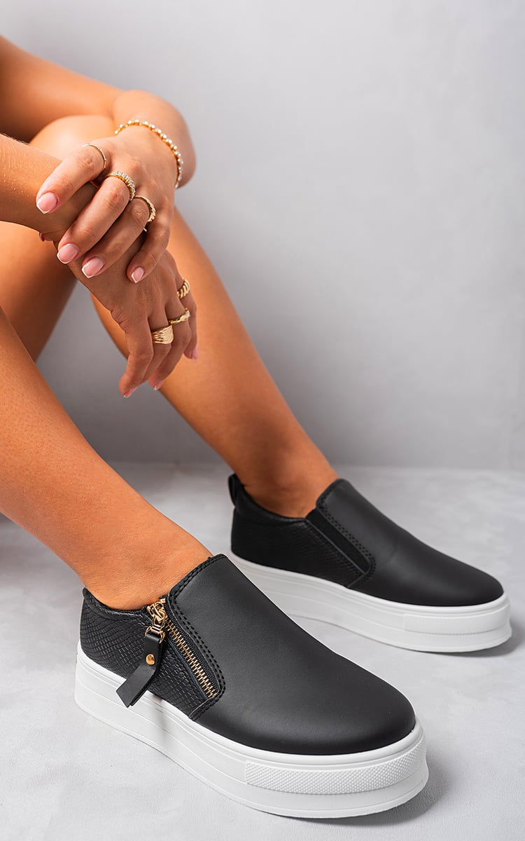 Black slip-on trainers with side zipper detail, gold-tone accents, and cushioned collar