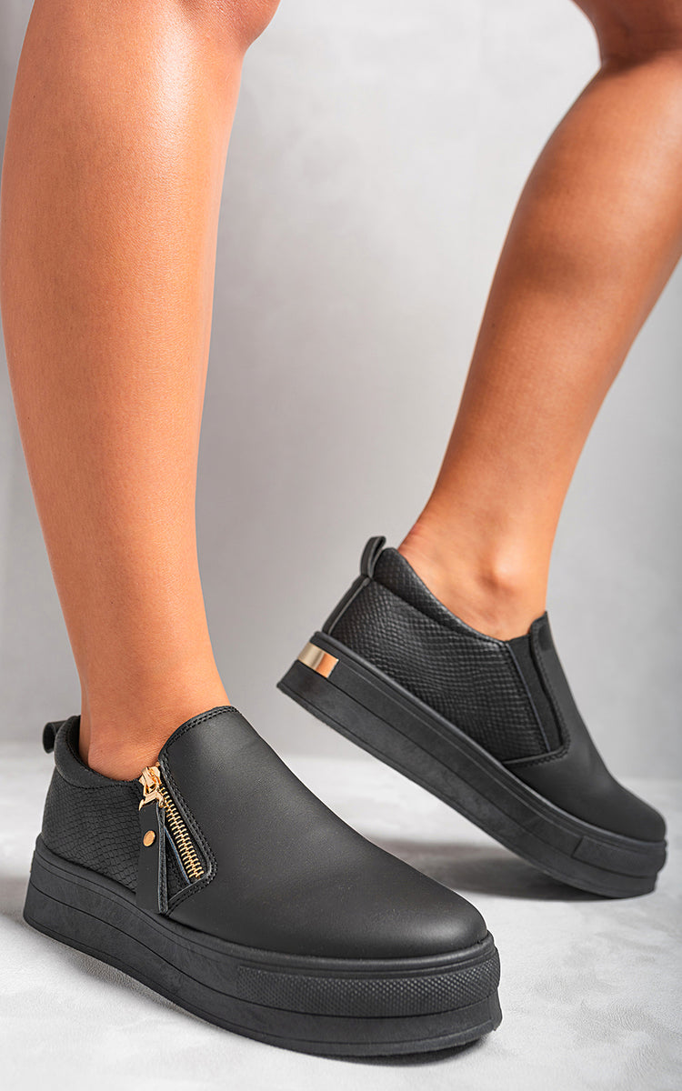 Black slip-on trainers with side zipper detail and gold-tone hardware on chunky sole