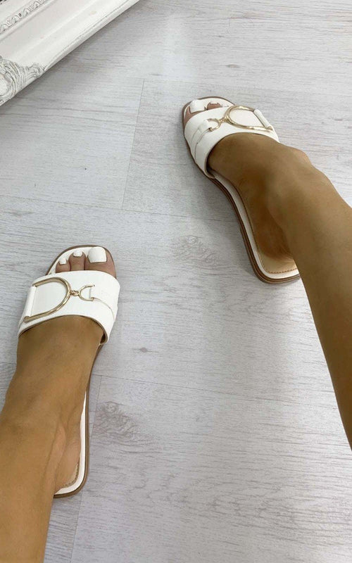 White slide sandals with wide straps and gold-tone ring detail, worn