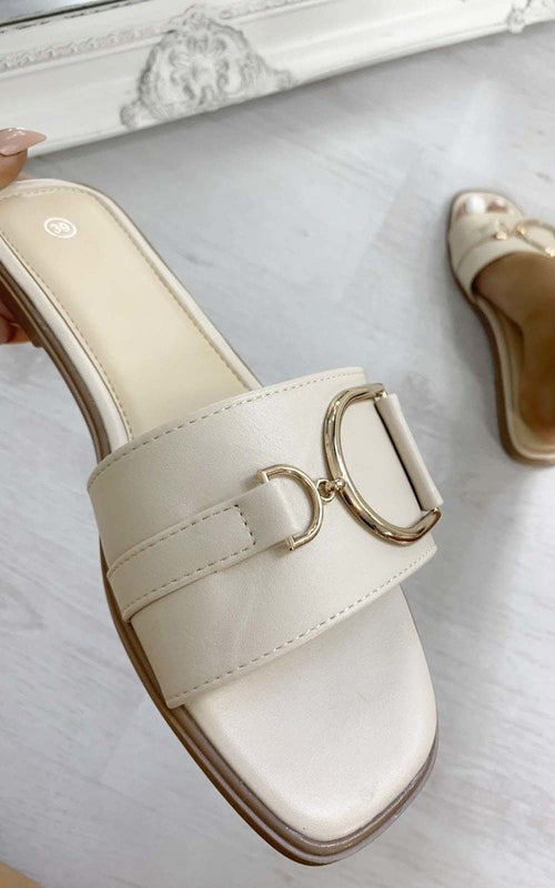 Cream slide sandals with wide strap and gold-tone ring buckle detail, close-up