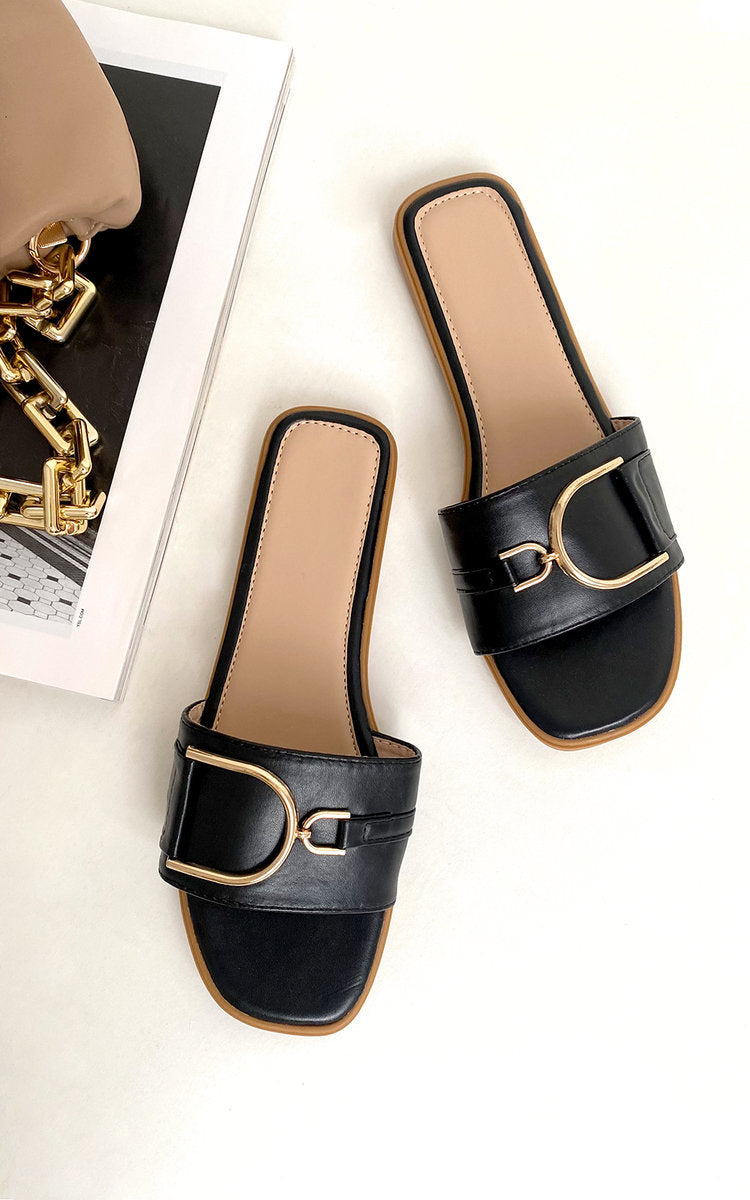 Black slide sandals with wide straps and gold-tone ring detail, front angle