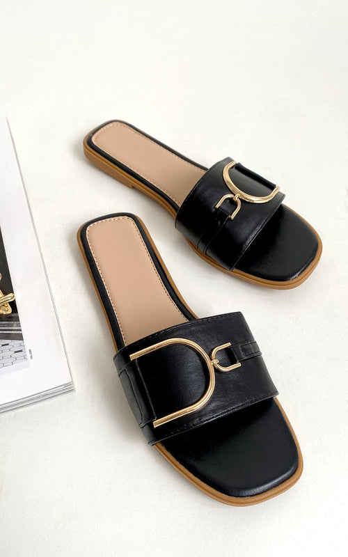 Black slide sandals with wide strap and gold-tone ring buckle detail, pair view