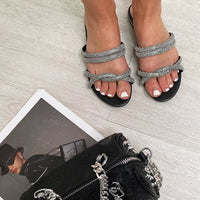 Black flat slip-on sandals with silver woven straps and open-toe design