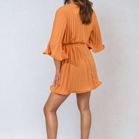 Orange pleated mini dress with tie waist and wide sleeves, gathered skirt.