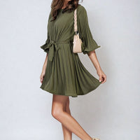 Olive green pleated mini dress with tie waist and wide sleeves, flared pleated skirt.