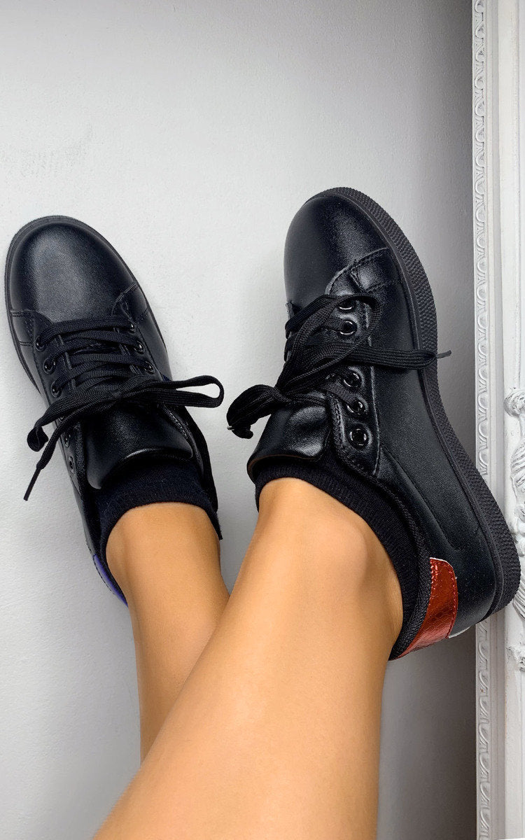 Black lace-up trainers on feet, with orange-red side stripe and white sole