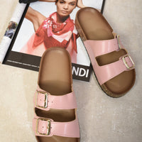 Pink slide sandals with double buckle straps and cork-effect soles, pair on floor