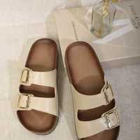 Cream slide sandals with double buckle straps and cork-effect soles, pair shown