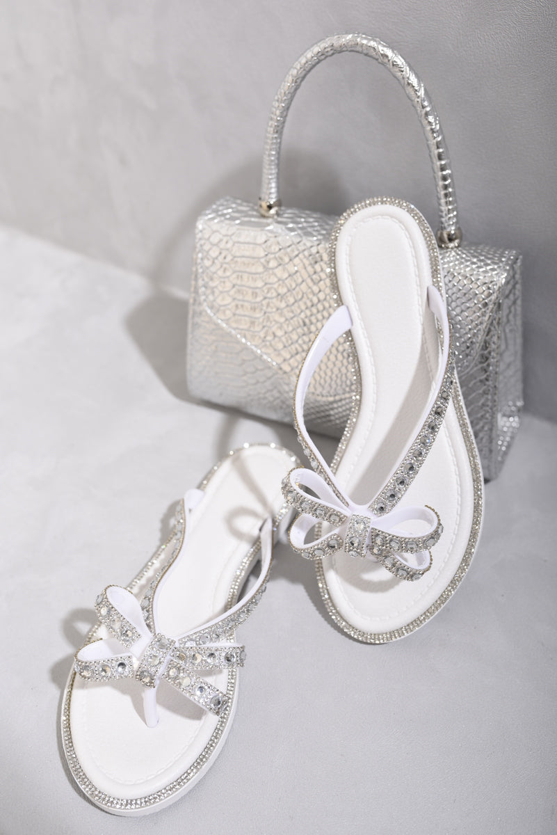 White flat thong sandals with jeweled bow and silver-trimmed edges