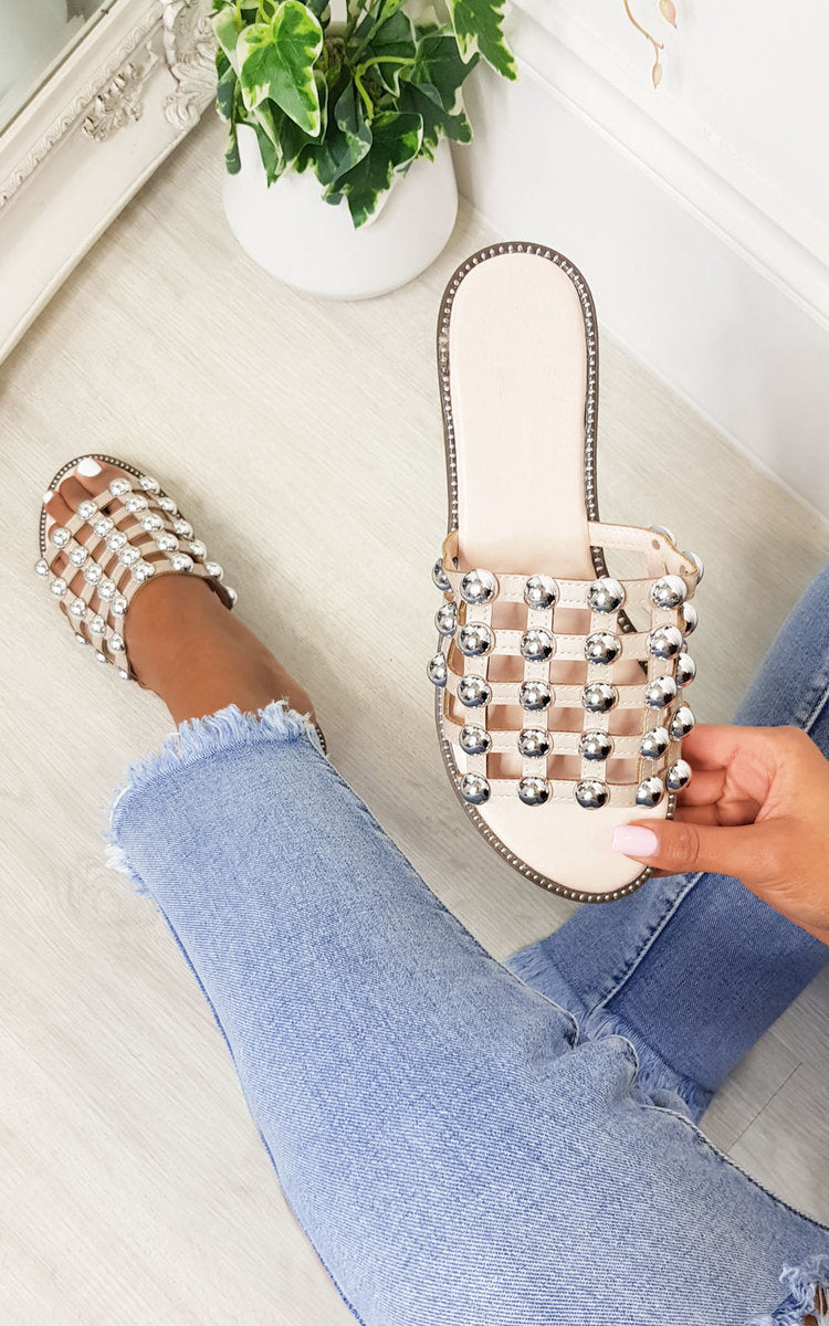 Nude flat slide sandals with studded lattice straps and rhinestone studs, angled view