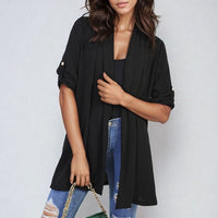 Black open-front cardigan with short sleeves and side pockets, draped over jeans