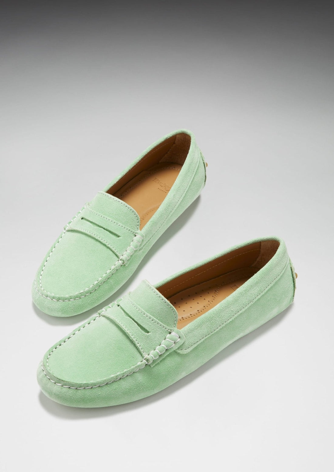Pair of green suede penny driving loafers with tan insoles and stitched apron toes.