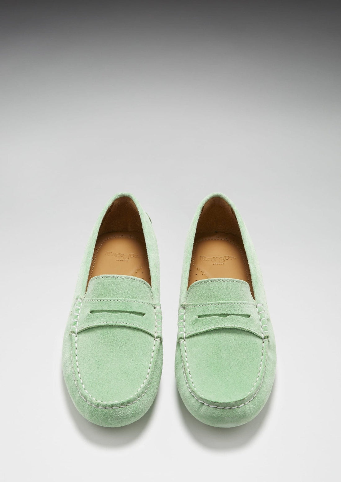 Pair of green suede loafers shown from above, with penny straps and stitched apron toes.