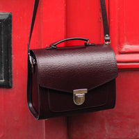 Marsala red leather satchel with top handle, shoulder strap, and front buckle clasp