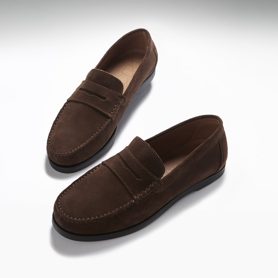 Pair of brown suede loafers with stitched toes, penny straps, and black soles