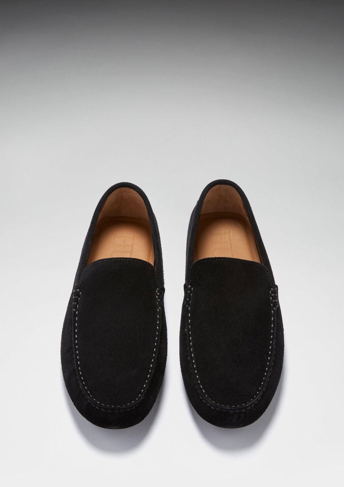 Pair of black suede driving loafers viewed from above, with tan leather lining and stitched trim.