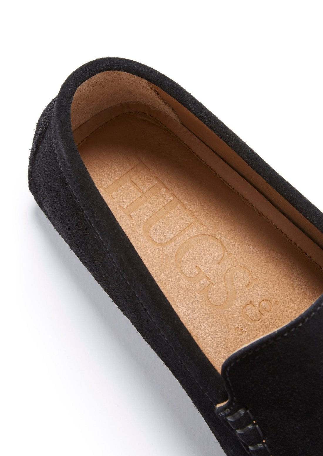Black suede loafer close-up showing the tan leather insole embossed with Hugs & Co.